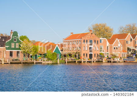 Netherlands traditional dutch houses on zaan river bank in holland, scenic waterfront view of beautiful old historic brick and green wooden buildings reflected in canal water under blue sky in zaandam Netherlands traditional dutch houses on zaan river bank in holland, scenic waterfront view of beautiful old historic brick and green wooden buildings reflected in canal water under blue sky in zaandam 140302184