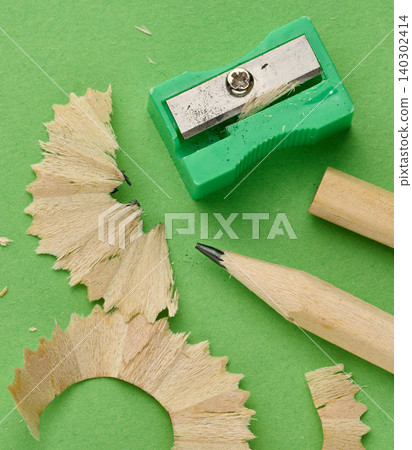 Green plastic pencil sharpener, sharp wooden pencil and figured shavings on green background, top view, preparation for drawing concept Green plastic pencil sharpener, sharp wooden pencil and figured shavings on green background, top view, preparation for drawing concept 140302414
