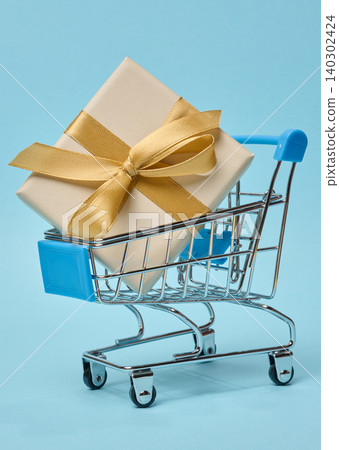 Miniature shopping cart with  gift box, beige packaging, blue background 140302424