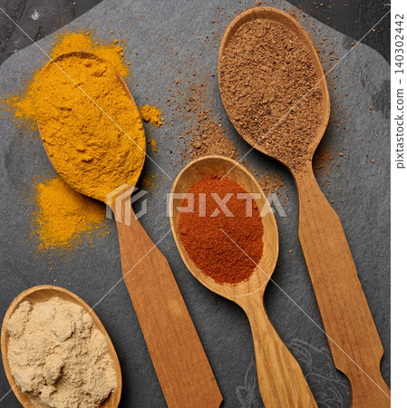 Multicolored ground spices in wooden spoons on a black board, 140302442