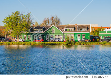 Traditional green dutch houses in zaandam near zaanse schans, beautiful waterfront panorama of historical holland architecture on zaan river bank reflected in canal water under clear blue sky, travel Traditional green dutch houses in zaandam near zaanse schans, beautiful waterfront panorama of historical holland architecture on zaan river bank reflected in canal water under clear blue sky, travel 140302736