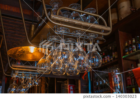 Amsterdam, Netherlands, 22.04.2026 - Wine glasses hanging on rack over a bar counter in a traditional dutch pub interior in zaandam, cozy warm light illumination in restaurant evening atmosphere Amsterdam, Netherlands, 22.04.2026 - Wine glasses hanging on rack over a bar counter in a traditional dutch pub interior in zaandam, cozy warm light illumination in restaurant evening atmosphere 140303023