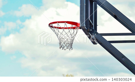 Outdoor basketball hoop with red rim against a blue sky with white clouds. Outdoor basketball hoop with red rim against a blue sky with white clouds. 140303024