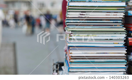 Stack of colorful books laying on a street vendor's stall with blurred people walking in the background Stack of colorful books laying on a street vendor's stall with blurred people walking in the background 140303263