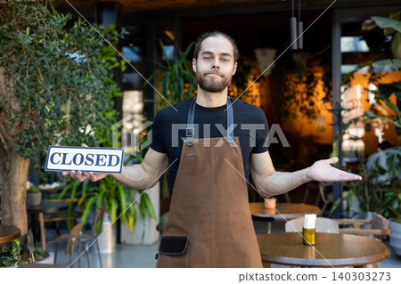 Disappointed waiter holding closed sign and shrugging 140303273