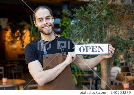 Cheerful cafe employee holding open sign and smiling Cheerful cafe employee holding open sign and smiling 140303279