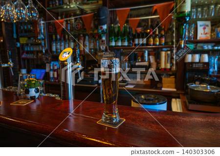 Amsterdam, Netherlands, 22.04.2026 - Hertog jan beer glass on wooden counter in traditional dutch bar interior, pint of draft lager on coaster with illuminated beer tap dispenser on background Amsterdam, Netherlands, 22.04.2026 - Hertog jan beer glass on wooden counter in traditional dutch bar interior, pint of draft lager on coaster with illuminated beer tap dispenser on background 140303306