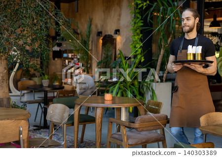 Professional waiter standing with tray in green restaurant 140303389