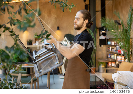 Male waiter organizing furniture and setting up cafe Male waiter organizing furniture and setting up cafe 140303476