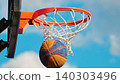 Basketball swishes through the net of an orange hoop against a bright blue sky 140303496