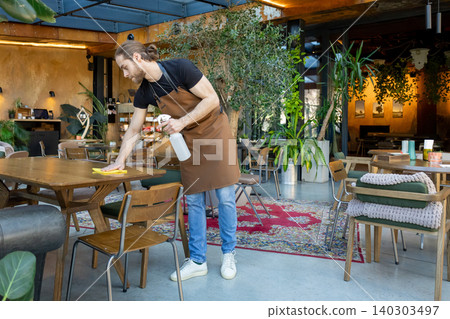 Employee wiping wide wooden table in cafe Employee wiping wide wooden table in cafe 140303497