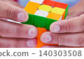Close up of male hands solving a colorful combination puzzle cube 140303508