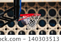 Basketball swishing through a red hoop and net on an outdoor court with a blurred background 140303513