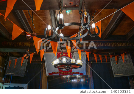 Amsterdam, Netherlands, 22.04.2026 - Ajax amsterdam football club flag in traditional dutch bar interior decorated with festive orange bunting flags, vintage wrought iron chandeliers hanging from wood 140303521