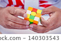 Close up of a man's hands solving a colorful combination puzzle cube against a blurred background 140303543