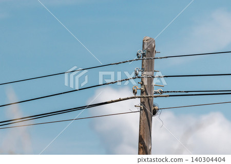 Wooden utility pole with overhead power lines against cloudy sky, electrical distribution infrastructure Wooden utility pole with overhead power lines against cloudy sky, electrical distribution infrastructure 140304404
