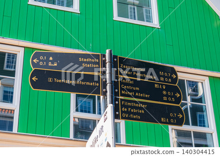 Amsterdam, Netherlands, 22.04.2026 - Tourist directional signpost in Zaandam city center pointing to local landmarks and station, street pedestrian navigation guide in front of green wooden facade 140304415