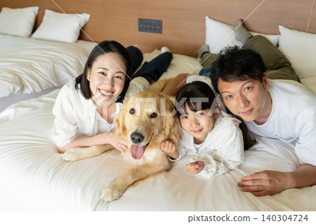 一個年輕的家庭和他們的狗躺在床上。 一個年輕的家庭和他們的狗躺在床上。 140304724