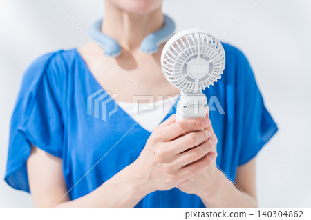 A woman using an ice ring and a handheld fan in the summer. A woman using an ice ring and a handheld fan in the summer. 140304862