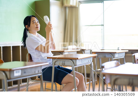 A high school girl using a fan in the classroom. A high school girl using a fan in the classroom. 140305509