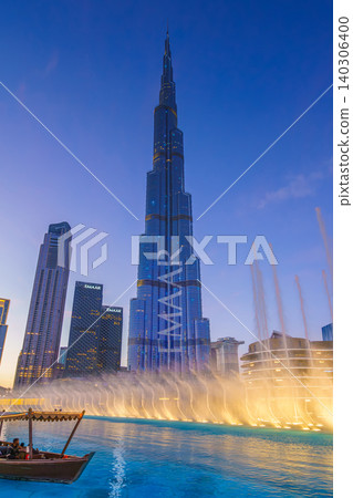 Dubai, United Arab Emirates - Jan 19 2024, vertical view of the Burj Khalifa Tower from below, with boat on foreground and dancing fountains, at evening with illumination, Dubai, UAE 140306400
