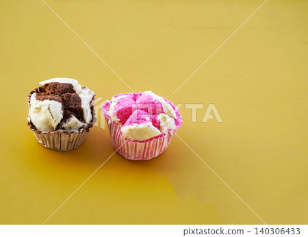 Two pieces of traditional Indonesian steamed cakes, featuring chocolate and pink known as kue apem, arranged on a bright yellow background. 140306433