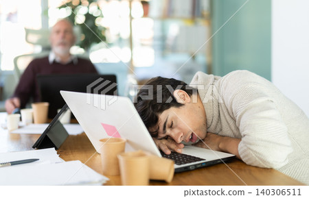 Wearied senior man and guy colleagues are dozing near workplace in office Wearied senior man and guy colleagues are dozing near workplace in office 140306511