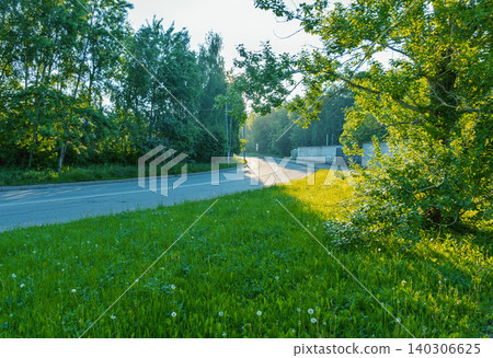 Sunlit country road bending through green meadow and trees Sunlit country road bending through green meadow and trees 140306625