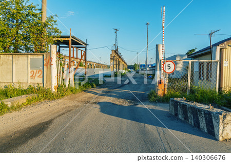 Industrial site gate with dirt road and speed limit sign at sunset 140306676