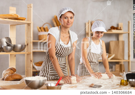 Two bakery employees work together to prepare dough for baking baguettes and croissants Two bakery employees work together to prepare dough for baking baguettes and croissants 140306684