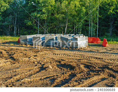 Stacked concrete curbs and road barriers on sandy construction site near forest Stacked concrete curbs and road barriers on sandy construction site near forest 140306689