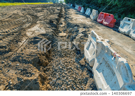 Construction site trench with gravel and plastic barriers along a rural road Construction site trench with gravel and plastic barriers along a rural road 140306697
