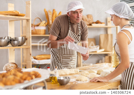 Male baker and teenage girl are looking at paper Male baker and teenage girl are looking at paper 140306724
