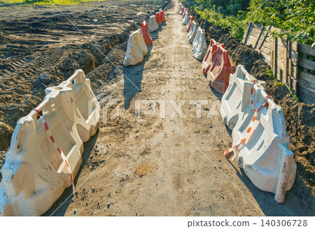 Dirt pathway bordered by alternating white and orange plastic barriers on a sunny day 140306728