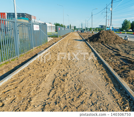 Construction site pathway with dirt base and curbstones alongside industrial fence Construction site pathway with dirt base and curbstones alongside industrial fence 140306750