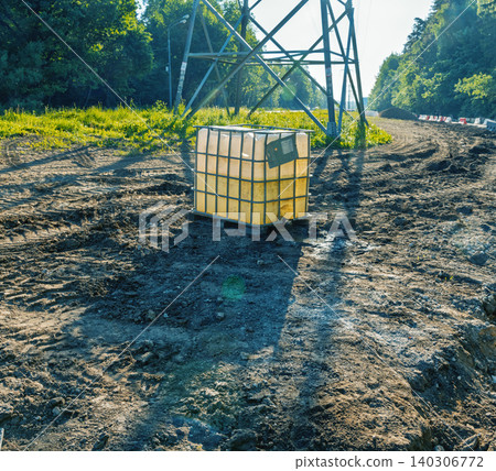 Plastic intermediate bulk container on muddy construction clearing under electricity pylon Plastic intermediate bulk container on muddy construction clearing under electricity pylon 140306772