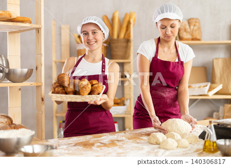 Female bakers rolling out dough and chatting Female bakers rolling out dough and chatting 140306817