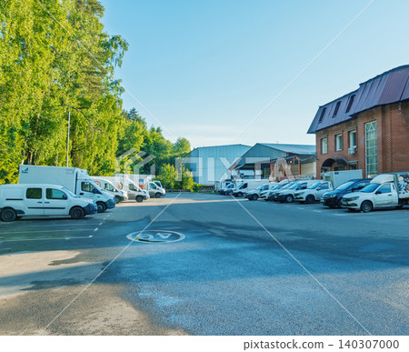 Delivery vans and service vehicles parked in industrial lot beside brick building and trees Delivery vans and service vehicles parked in industrial lot beside brick building and trees 140307000