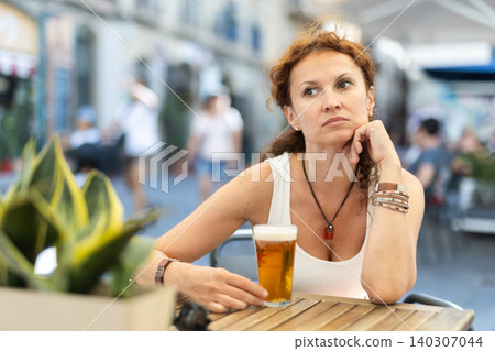 Thoughtful middle-aged woman drinking beer in open-air cafe Thoughtful middle-aged woman drinking beer in open-air cafe 140307044