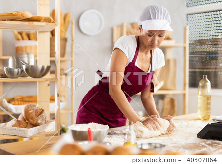 Working in bakery - woman kneads raw dough to make baguettes or croissants 140307064