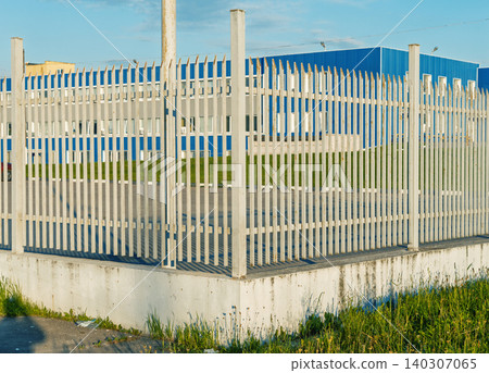White metal security fence around blue industrial building under clear sky White metal security fence around blue industrial building under clear sky 140307065