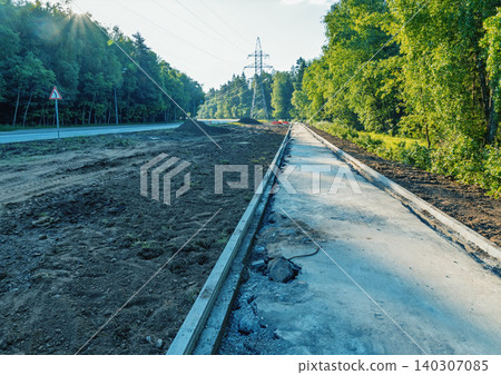 Newly paved roadside sidewalk beside forested highway with utility tower 140307085
