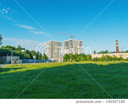Unfinished residential towers with construction crane behind grassy field under blue sky Unfinished residential towers with construction crane behind grassy field under blue sky 140307180