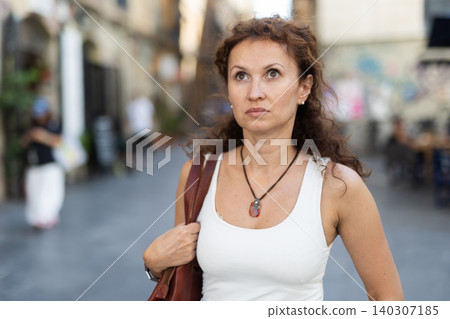 Serious middle-aged woman walking along square Serious middle-aged woman walking along square 140307185