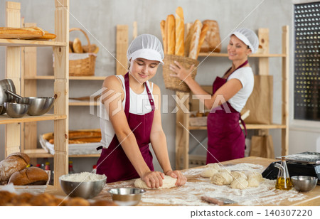 Two women prepare dough and take hot baguettes out of the oven - work in bakery Two women prepare dough and take hot baguettes out of the oven - work in bakery 140307220