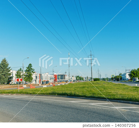 Suburban road median with power lines and commercial buildings under clear blue sky Suburban road median with power lines and commercial buildings under clear blue sky 140307256