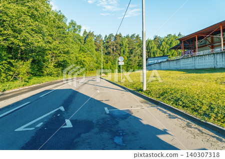 Empty suburban road curving past grassy embankment and forest Empty suburban road curving past grassy embankment and forest 140307318
