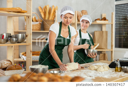Two bakers knead dough in a bakery 140307417
