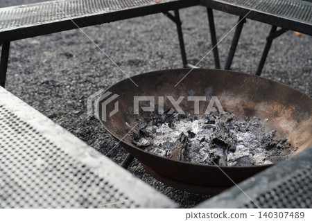 The ashes and charcoal remaining in the fire pit signal the end of the camping trip. The ashes and charcoal remaining in the fire pit signal the end of the camping trip. 140307489