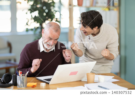 Happy young and elderly men colleagues cheering at successful result on laptop Happy young and elderly men colleagues cheering at successful result on laptop 140307532